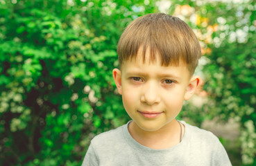 Serious boy in bright green garden. Adorable cute kid with stylish hair dress standing in bright greenery in street