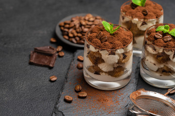 Classic tiramisu dessert in a glass on stone serving board on dark concrete background