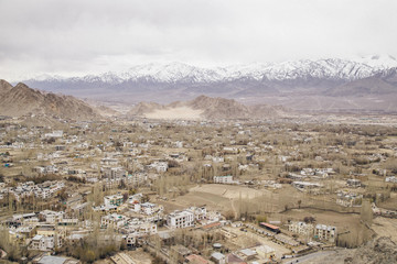 Fototapeta premium Leh Ladakh city view from Shanti Stupa. Beautiful amazing village in the valley with snow mountain at background. Ladakh, India.