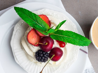 Dessert pavlova meringue with whipped cream and mint leaf decoration and cup of coffee