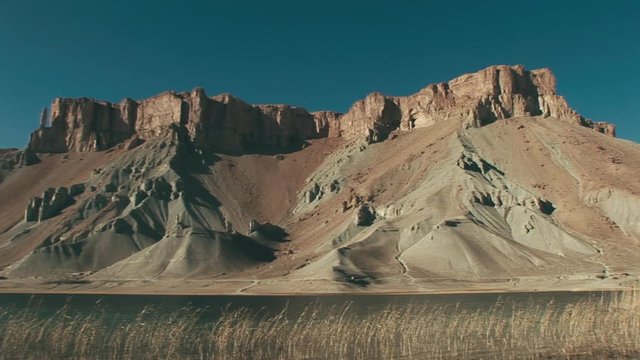 Panning shot of the Travertine Rock Formations And Turquoise Blue Lake of Band-e Amir National Park, Afghanistan with Phragmites swaying in the wind