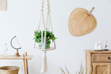 Stylish and minimalistic boho interior with design and handmade macrame shelf planter hanger for indoor plants, wooden furnitures, elegant accessories ,rattan basket and leaf. Cozy home decor.