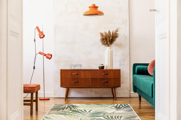 Stylish compositon of retro home interior with vintage cupboard, velvet sofa, flowers in vase, design orange lamps , elegant accessories and abstract paintings. Minimalistic concept. Nice home decor. 