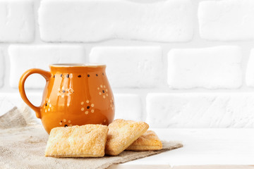 Rustic cup with cookies on white brick wall background.