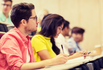 education, high school, university, learning and people concept - group of international students with notebooks writing in lecture hall and talking