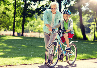 family, generation, safety and people concept - happy grandfather teaching boy how to ride bicycle...