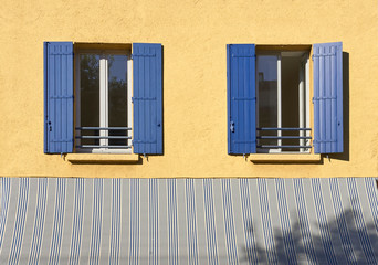 Two windows with blue shutters in a yellow wall in the Provence France during Summer