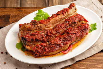 Grilled pork ribs in spicy sauce with tomatoes. Ketogenic and paleo food. Large portion on a white plate. Close up and horizontal orientation.