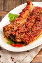 Grilled pork ribs in spicy sauce with tomatoes. Ketogenic and paleo food. Large portion on a white plate. Close up and vertical orientation. .