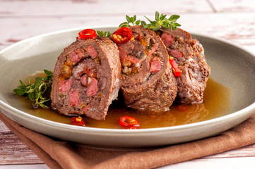 Beef tenderloin rolls stuffed. Slices of meat served on a plate in a sauce and with fresh vegetables and herbs. Close up and horizontal orientation.