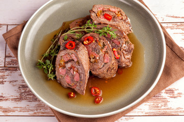 Beef tenderloin rolls stuffed. Slices of meat served on a plate in a sauce and with fresh vegetables and herbs. Close up and horizontal orientation.