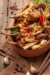 Fried lamb chops with fried onions, garlic and fresh herbs. A large portion is served on a clay plate and decorated in a rustic style. Close up and vertical orientation.