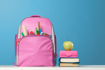 Student set. Pink backpack with stationery, a stack of books, a lunchbox, an apple on the table on a blue background. Back to school. - Powered by Adobe