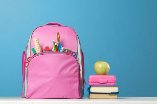 Student Set. Pink Backpack With Stationery, A Stack Of Books, A Lunchbox, An Apple On The Table On A Blue Background. Back To School.