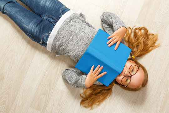 Cute little girl in glasses with a book lying on the floor
