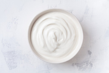 Greek yogurt in bowl on white stone table top view.