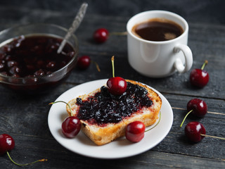 White Cup of coffee and toast with cherry jam on white plate on black table