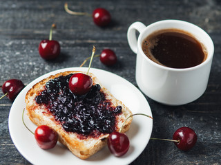 White Cup of coffee and toast with cherry jam on white plate on black table