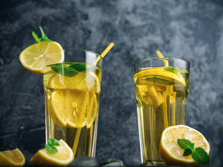 Traditional iced, lemon and mint iced tea . Mojito in two glass glasses on a dark concrete table