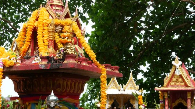 Wooden miniature guardian spirit house. Small buddhist temple shrine, colorful flower garlands. San phra phum erected to bring fortune. Traditional respect animistic rituals, pray ceremonies