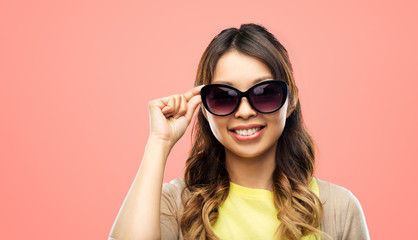 summer fashion, style and eyewear concept - happy smiling young asian woman in sunglasses over living coral background