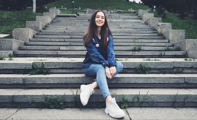 Fototapeta premium Lifestyle fashion stylish teenager sits on the steps in the city park in denim clothes