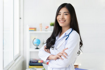 Asian female doctor work at hospital office desk giving patient convenience online service advice, smiling write a prescription to order medical, cross arm, health care and preventing disease concept.