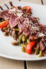 Sliced medium rare Roast beef with pickles, cherry tomatoes,mushrooms on a white plate on wooden background.