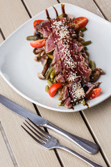Sliced medium rare Roast beef with pickles, cherry tomatoes,mushrooms on a white plate on wooden background.