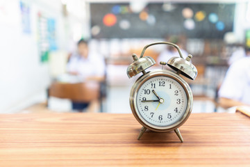 Test Examination in Education concept,Alarm clock on wooden table,students exams in a classroom background ,Scholarship tests for study abroad