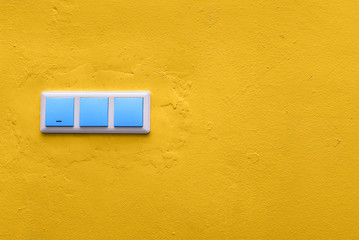 Blue switches on a yellow concrete wall. Colorful electrical switch. Creative style. Copy space