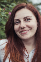 Fototapeta premium Red haired girl smiling at the camera in the botanical garden