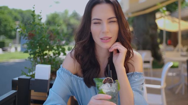 Beauiful woman sitting in outdoor restaurant and sip mojito dring in summer hot day