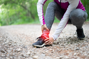 sport runner woman cramps in leg and feel pain, athletic young Asian girl in sportswear touching her muscles ankle painful injury outside after exercise workout in nature road. Sports injuries concept