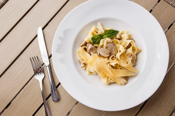 Tagliatelle vegetarian Pasta Dish with Mushrooms decorated with basil. Delicious lunch with pasta and white mushrooms. On wooden background.
