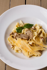 Tagliatelle vegetarian Pasta Dish with Mushrooms decorated with basil. Delicious lunch with pasta and white mushrooms. On wooden background.