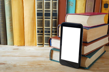 mobile phone with white screen for copy space and book pile on wooden background, e-learning concept