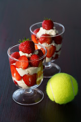 Whipped cream and strawberries served in a glass. Dark wooden table, tennis ball, high resolution