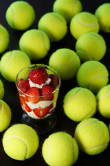 Whipped cream and strawberries served in a glass. Dark wooden table, tennis ball, high resolution