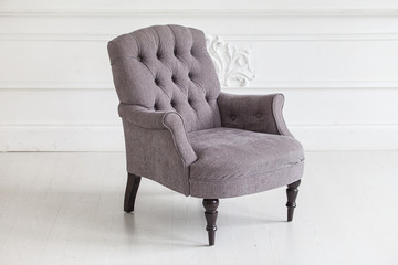 Living room in the Rococo style. Vintage grey armchair against the wall with plaster stucco patterns. Selective focus.