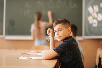 Group of school kids with pens and notebooks writing test in classroom. education, elementary school, learning and people concept