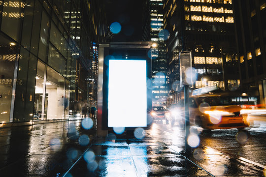 Bus Station Billboard In Rainy Night With Blank Copy Space Screen For Advertising Or Promotional Content, Empty Mock Up Lightbox For Information, Blank Display In Urban City Street With Long Exposure