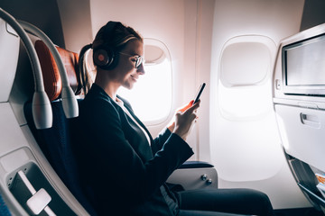Side view of smiling female travelling via popular airlines sitting in business class and enjoying...
