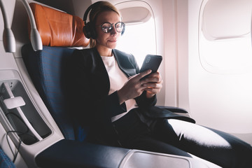 Caucasian woman dressed in formal wear use mobile phone inside airplane sitting on passenger seat,...