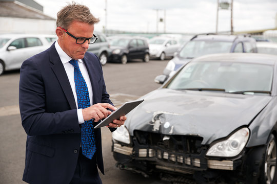 Male Insurance Loss Adjuster With Digital Tablet Inspecting Damage To Car From Motor Accident