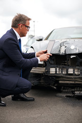 Male Insurance Loss Adjuster With Digital Tablet Inspecting Damage To Car From Motor Accident