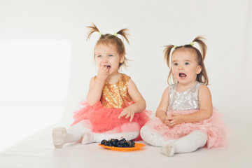 two little girls eating grapes sitting on the floor on a white background