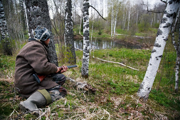 Hunter with a gun sitting in ambush in the woods. Waiting for game. Siberia