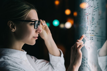 Digital monitor with public transport subway map. Female standing at big display with advanced innovative technology. Young woman touching with finger sensitive screen while selecting surface option