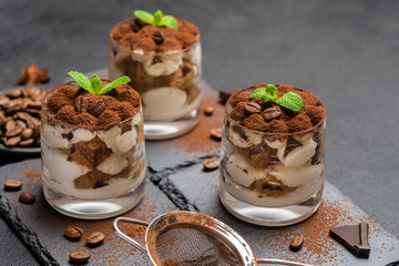 Classic tiramisu dessert in a glass on stone serving board on dark concrete background